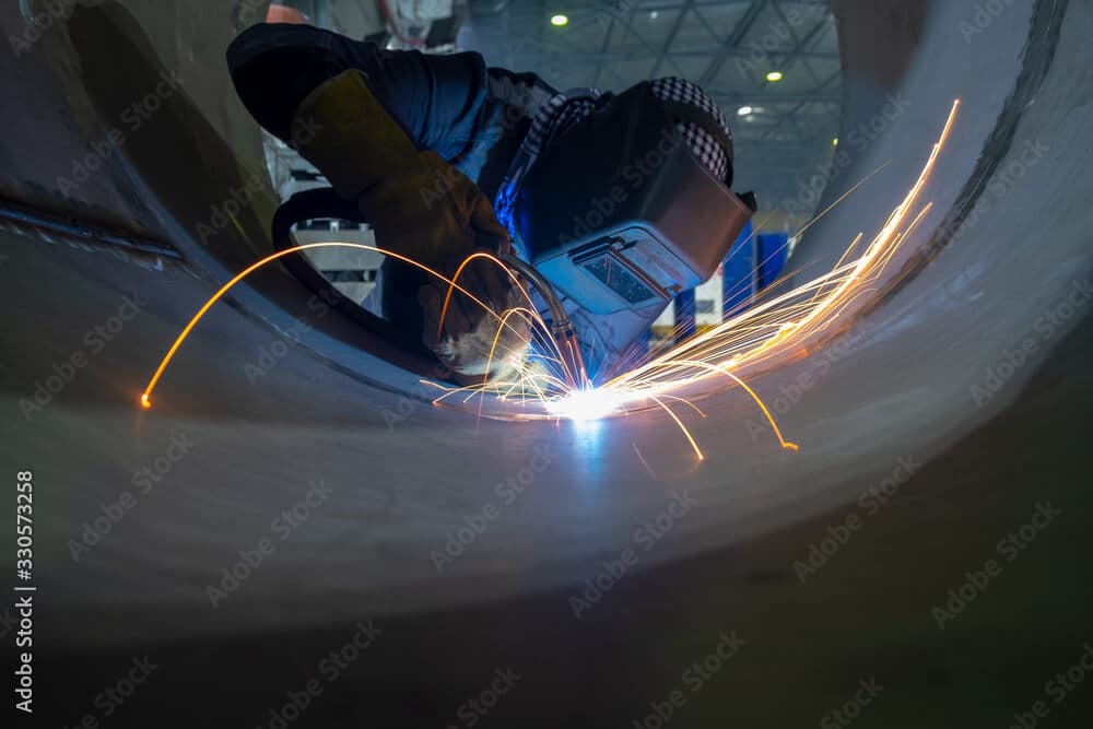 Schweißer bearbeitet Metallrohr mit Funken in Fabrikumgebung.