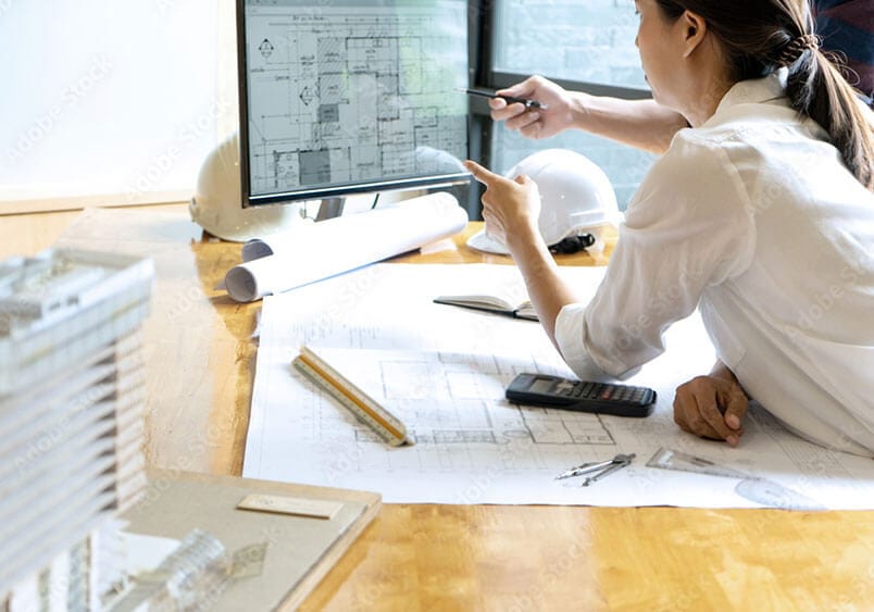 Architekten analysieren Baupläne am Schreibtisch, mit Computer und Bauzeichnungen für ein Architekturprojekt.