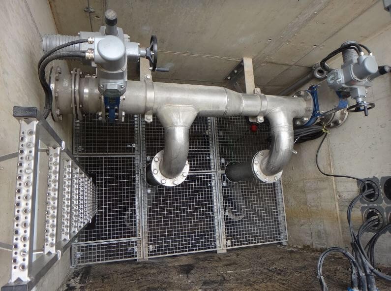 Industrieventil mit Rohrleitungen und Gittern in technischem Raum aus Edelstahl, Nahaufnahme.