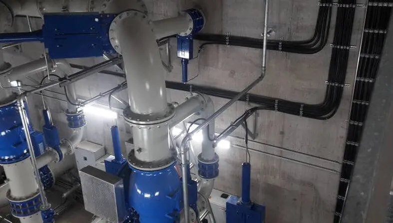 Industrieleitungen und Kabel in grauem Raum, beleuchtet, mit blauen Armaturen und Verbindungen.