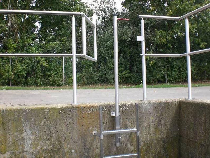 Metallgeländer und Leiter an einem Betonbecken vor Bäumen. Sicherheitseinrichtung in einer Außenanlage.