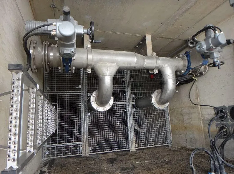 Industrieventil mit Rohrleitungen und Gittern in technischem Raum aus Edelstahl, Nahaufnahme.