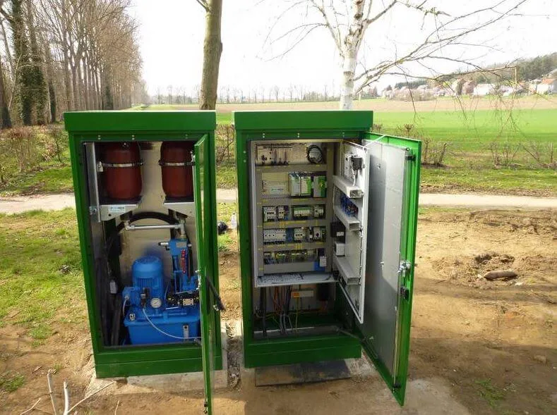 Zwei geöffnete grüne Stromkästen im Freien, zeigen technische Geräte und Schaltungen bei sonnigem Wetter.
