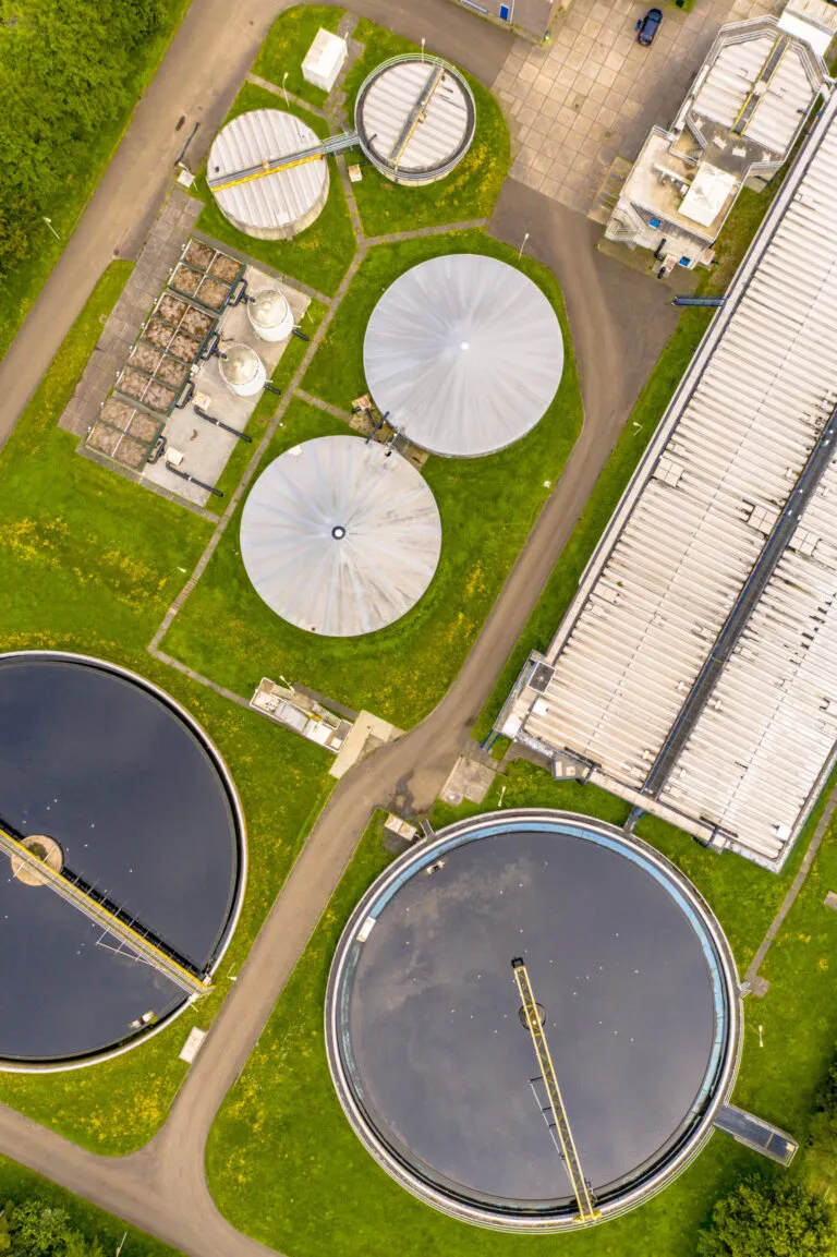 Luftbild einer Kläranlage mit runden Becken und grünen Flächen.