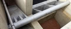 Stauklappe mit Betonwänden und großem Metallrohr in urbaner Umgebung.